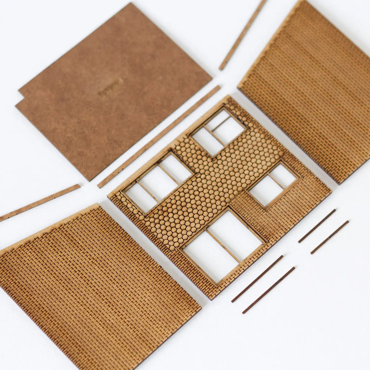 Rail Model Terraced House 4 mm scale kit—flat-lay of unassembled laser-cut MDF parts: roof panel, textured brick side walls, front wall with hexagonal-tile and brick detail, rear wall, and narrow structural strips, all arranged neatly on a white background.