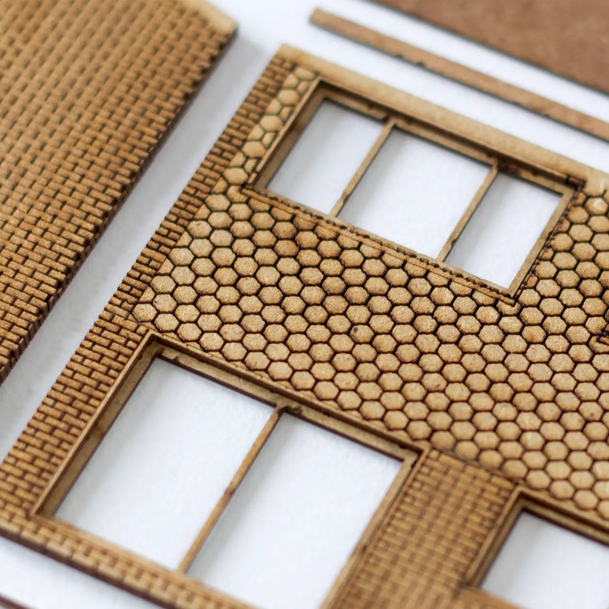Close-up of Rail Model Terraced House 4 mm scale kit parts—laser-cut MDF wall sections with fine brick courses, hexagonal-tile cladding, and precise window openings, shown unassembled on a white background.