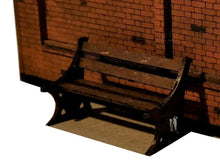 Load image into Gallery viewer, A model of a station platform bench made from MDF, painted and placed on a layout with a brick wall in the background.