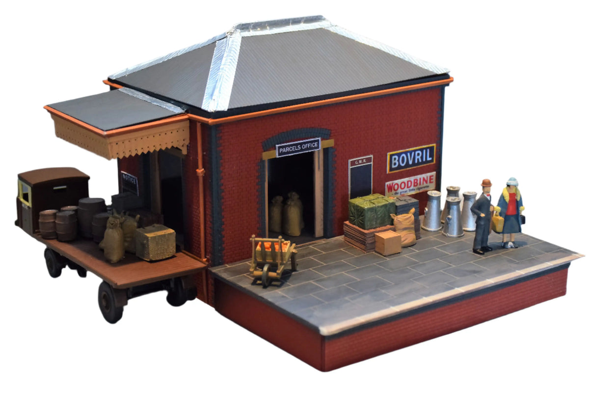 Rail Model Rhoystellen Station Goods Shed, 4 mm scale—fully assembled and detailed diorama featuring a red-brick GWR parcels office with pitched roof, loading canopy, signage, milk churns, crates, sacks, and miniature figures on a raised platform alongside a delivery cart.
