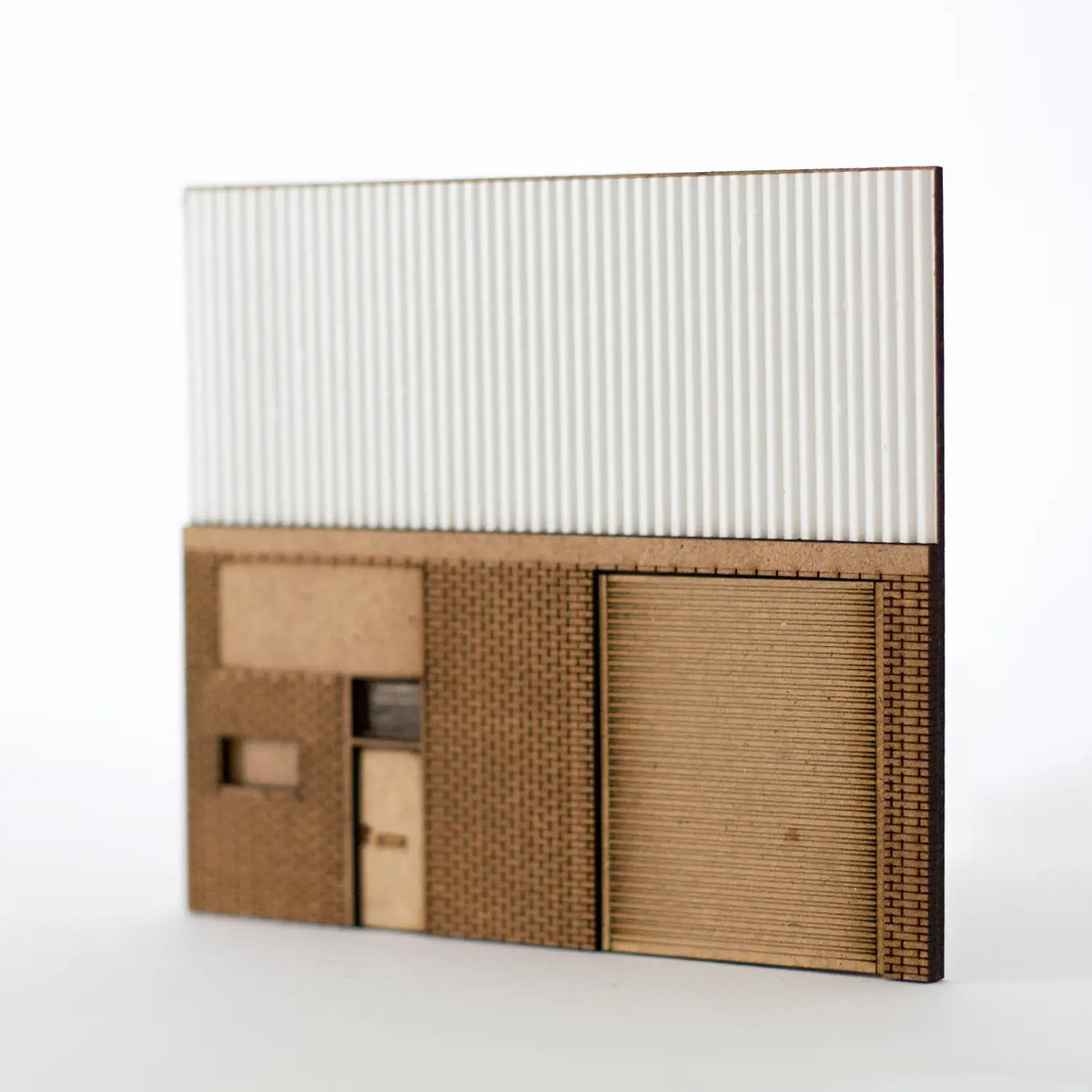 Rail Model Light Industrial Unit Relief, 4 mm scale—laser-cut MDF and plastic panel featuring brick-textured lower wall with roller shutter door, personnel door, and windows, topped with corrugated cladding to represent a modern commercial facade.