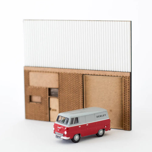 Rail Model Light Industrial Unit Relief, 4 mm scale—partially assembled wall section featuring laser-engraved brickwork, roller shutter door, side access door, and corrugated cladding, shown with a scale model red-and-grey ‘Denley’ delivery van in front.