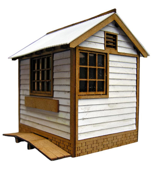 A model of a small ground frame hut with corrugated plastic roofing, wooden-like details, and a window with film applied to its panes.
