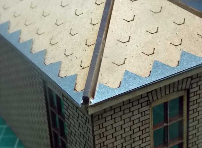 A close-up of a model train roof tile with a slate grey color, featuring a diamond pattern design, applied on a model roof.